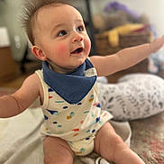 Miles is registered to the contest to win money with this photo: baby, infant, face, eyes, hair, bib, onesie, blanket, pillow, basket, stuffed_animal, living_room, indoor, sitting, smiling, happy, chubby_legs, bokeh, soft_light, portrait
