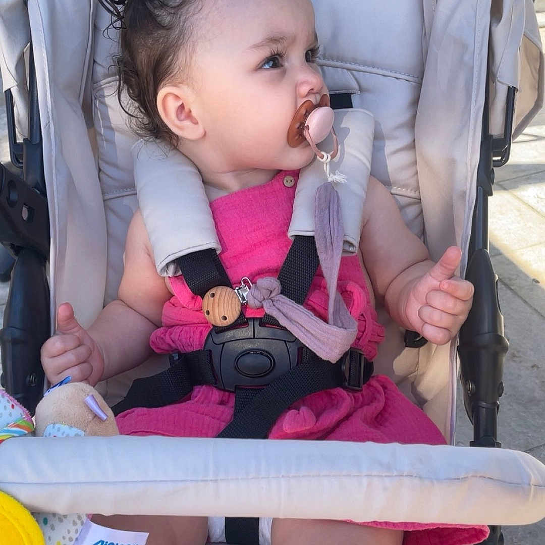 Havana a rejoint le concours — aidez-le/la à gagner de superbes lots ! baby, baby_toy, child, child_safety, clothing, curly_hair, cute, happy, infant, outdoor, pacifier, pink_dress, playful, portrait, seatbelt, sitting, stroller, sunlight, thumbs_up, toy