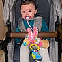 baby, stroller, pacifier, plush_toy, indoor, child, diaper_bag, pigtails, clothing, seatbelt, person, cute, infant, toy, baby_clothes, baby_accessories, colorful, sitting, young_child, baby_girl