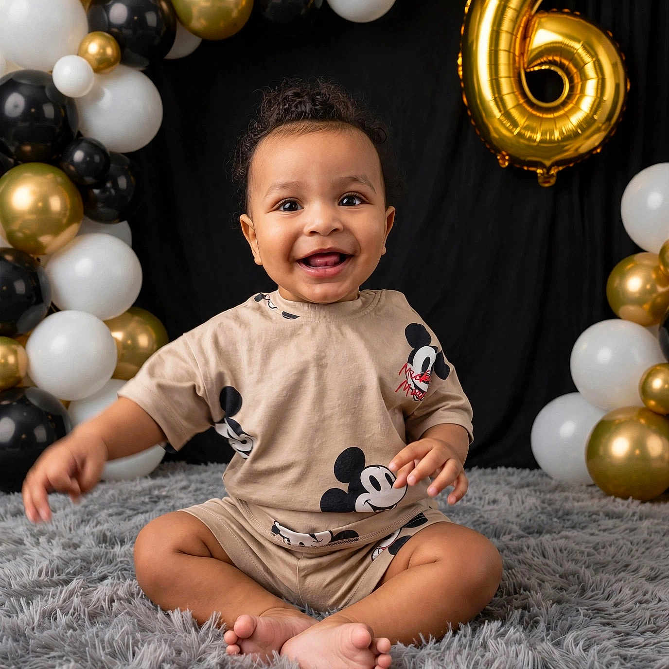 Decari is registered to the contest to win money with this photo: baby, child, smiling, sitting, mickey_mouse, balloons, birthday, gold_balloon, black_balloon, white_balloon, fluffy_rug, cute_clothing, happy, portrait, indoor, celebration, number_6, curly_hair, infant, young_child
