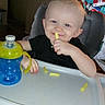 toddler, child, high_chair, snack, sippy_cup, blue, green, smile, indoor, home, toy, feeding, cute, person, baby, playful, seat, table, face, hair