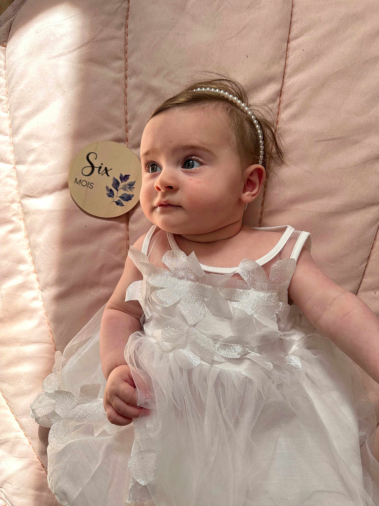 Louise participe au concours pour gagner de l'argent avec cette photo : baby, child, infant, dress, headband, pearl, pink, quilt, soft_light, wooden_plaque, six_months, curious, portrait, laying_down, flower_decorations, cute, indoors, skin, face, hand