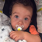Albin joined the competition — help win amazing prizes! baby, child, pacifier, blanket, car_seat, warning_labels, curly_hair, face, hand, orange_shirt, close_up, blue_eyes, infant, cute, sitting, indoor, soft_texture, portrait, young, cozy