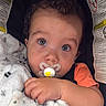 baby, child, pacifier, blanket, car_seat, warning_labels, curly_hair, face, hand, orange_shirt, close_up, blue_eyes, infant, cute, sitting, indoor, soft_texture, portrait, young, cozy
