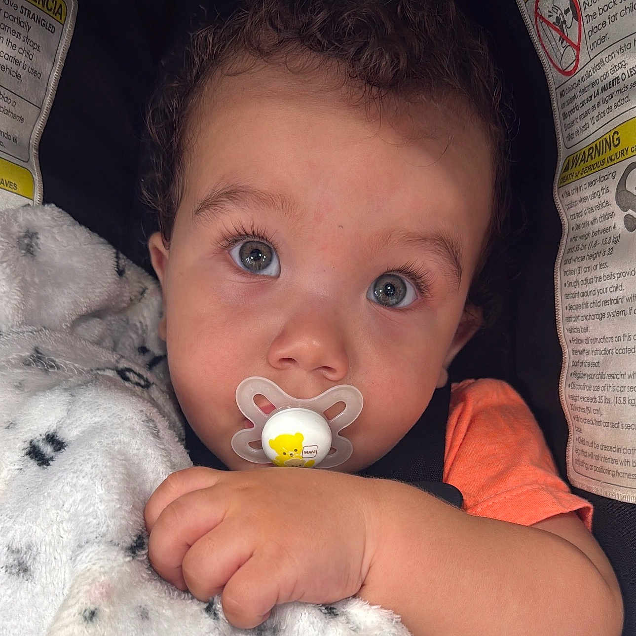 Albin joined the competition — help win amazing prizes! baby, child, pacifier, blanket, car_seat, warning_labels, curly_hair, face, hand, orange_shirt, close_up, blue_eyes, infant, cute, sitting, indoor, soft_texture, portrait, young, cozy