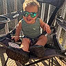 toddler, child, sunglasses, smile, chair, outdoor, sunlight, mesh_fence, tank_top, shorts, footwear, happy, baby, seat, casual, reflection, summer, cute, person, portrait
