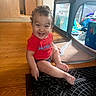 toddler, child, smiling, curly_hair, red_shirt, indoor, wooden_floor, playpen, toys, happy, person, baby, home, floor, sitting, laughing, casual_clothing, young_child, cute, portrait