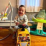 toddler, child, smiling, indoor, toy, yellow_bus, baby_gear, flooring, happy, playful, clothing, mickey_mouse, curtain, window, wooden_floor, person, cute, sitting, steering_wheel, fun