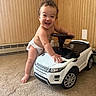 toddler, child, diaper, toy_car, range_rover, indoor, carpet, wood_paneling, smiling, happy, baby, cute, playing, steering_wheel, vehicle, small, car_toy, floor, wall, room