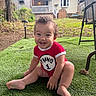 toddler, baby, smiling, sitting, grass, backyard, red_clothing, curly_hair, happy, outdoor, house, fence, chair, daylight, lawn, person, cute, child, playful, greenery