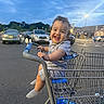 toddler, child, shopping_cart, walmart, parking_lot, smiling, happy, curly_hair, outdoor, evening, store, retail, person, clothing, socks, metal, vehicle, sky, urban, baby
