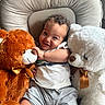baby, child, teddy_bear, stuffed_animal, curly_hair, smiling, cute, cushion, white_teddy, orange_teddy, ribbon, golden_bow, comfortable, indoor, happy, infant, soft_toys, playful, portrait, casual_clothing