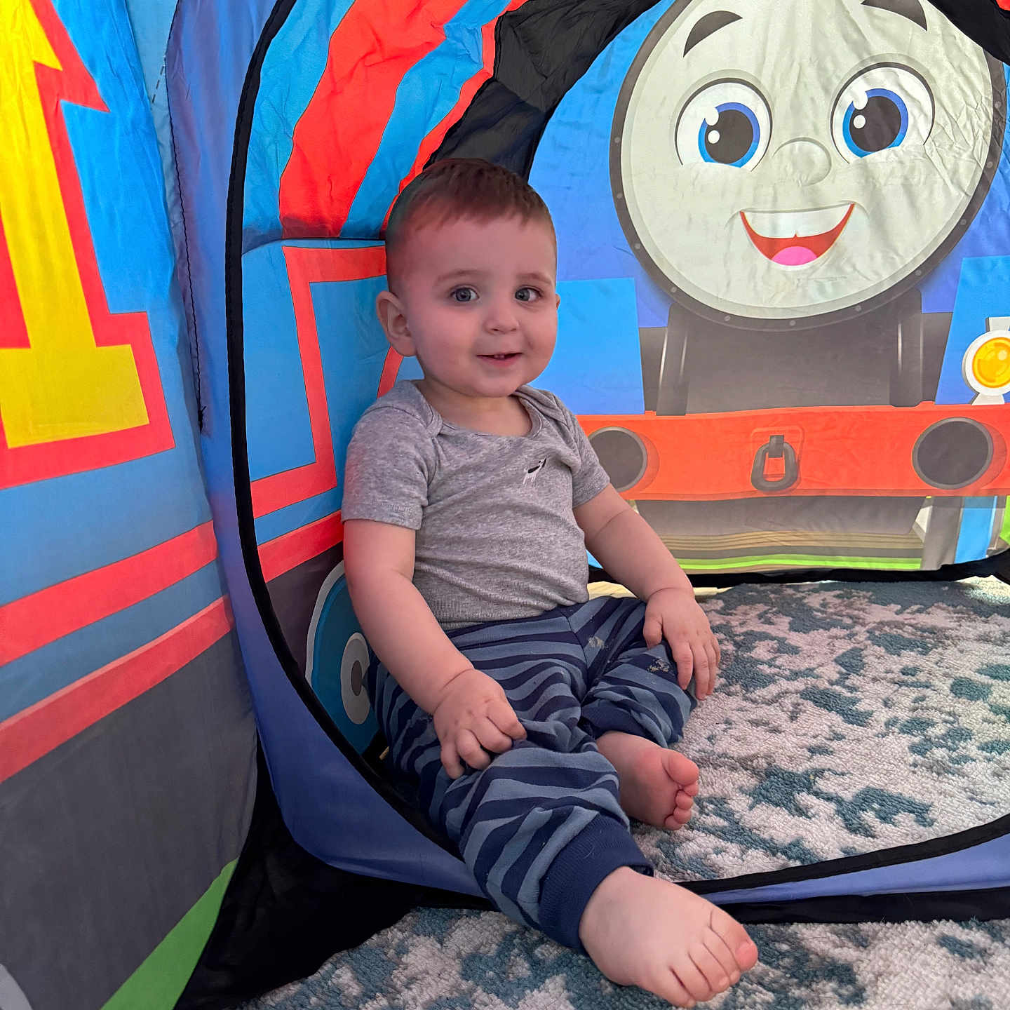 Jameson joined the competition — help win amazing prizes! blue, carpet, child, clothing, colorful, cute, face, foot, gray, happy, indoor, patterned, play_tent, red, sitting, smiling, striped_pants, toddler, toy, young