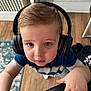 blue_shirt, carpet, casual_clothing, chair, child, curious, cute, expression, floor, furniture, hand, headphones, home, indoor, looking_up, person, portrait, toddler, wooden_floor, young_child