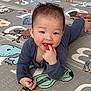 baby, child, infant, play_mat, floor, blue_clothing, finger_in_mouth, happy, smiling, cartoon_animals, letters, cute, indoors, young_child, playtime, lying_down, curious, joyful, head, face