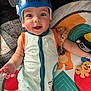 baby, helmet, smile, toy, play_mat, child, infant, colorful, cute, happy, lying_down, blue_helmet, onesie, indoors, face, expression, hand, arm, cheerful, bright