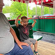 Daniel joined the competition — help win amazing prizes! child, boy, excited, sitting, bench, man, adult, pavilion, wooden_floor, greenery, outdoor, casual_clothing, shorts, tshirt, sandals, emotion, happy, family, portrait, daylight