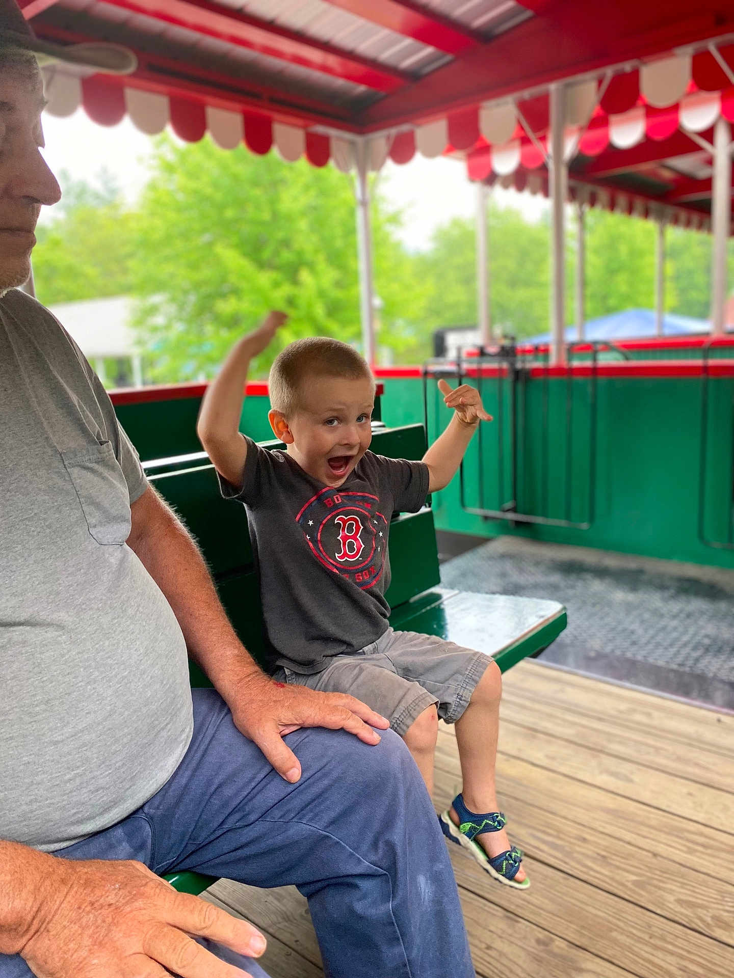 Daniel joined the competition — help win amazing prizes! child, boy, excited, sitting, bench, man, adult, pavilion, wooden_floor, greenery, outdoor, casual_clothing, shorts, tshirt, sandals, emotion, happy, family, portrait, daylight
