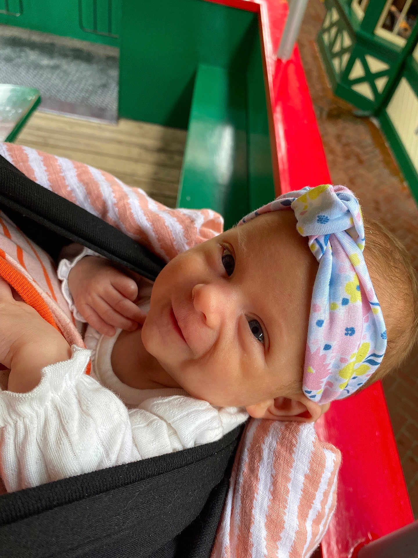 Sadie Mae is registered to the contest to win money with this photo: baby, infant, smile, headband, striped_blanket, baby_carrier, indoor, bench, wooden_floor, colorful, face, person, cute, portrait, child, happy, clothing, fabric, closeup, toddler