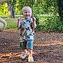 toddler, child, smiling, outdoor, playground, trees, sunlight, grass, leaves, dinosaur_shirt, plaid_shorts, crocs, happy, walking, nature, daylight, person, casual_clothing, young_child, park