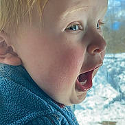 Abel Blake is registered to the contest to win money with this photo: child, blonde_hair, blue_eyes, side_profile, open_mouth, joyful_expression, blue_sweater, knitwear, window, snow, outdoor, winter, face, skin, eyelashes, ear, nose, cheeks, young, portrait