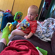 Abel Blake is registered to the contest to win money with this photo: blanket, casual, child, colorful, couch, cozy, doorway, floor, furniture, home, indoor, person, poster, relaxed, room, shirt, socks, toddler, toy, wall