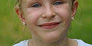 Rhyleigh-ann is registered to the contest to win money with this photo: child, girl, smile, face, blue_eyes, blonde_hair, earrings, white_shirt, paint_stains, outdoor, green_background, portrait, young, casual_clothing, natural_light, close_up, happy, primary_school, headshot, expression