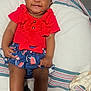 baby, smiling, red_clothing, blue_skirt, white_socks, blanket, striped_blanket, infant, happy, cute, sitting, indoors, child, person, face, head, legs, hand, comfort, portrait