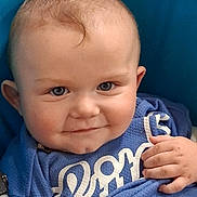 Maddox is registered to the contest to win money with this photo: baby, child, smiling, blue_eyes, curly_hair, blue_clothing, cute, portrait, infant, hand, face, happy, closeup, person, skin, eyebrows, sitting, indoors, expression, young