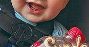 Kyler is registered to the contest to win money with this photo: baby, child, smiling, car_seat, seatbelt, drink_bottle, red, face, happy, indoors, portrait, young_child, cute, holding, close_up, expression, person, bottle, casual, daylight