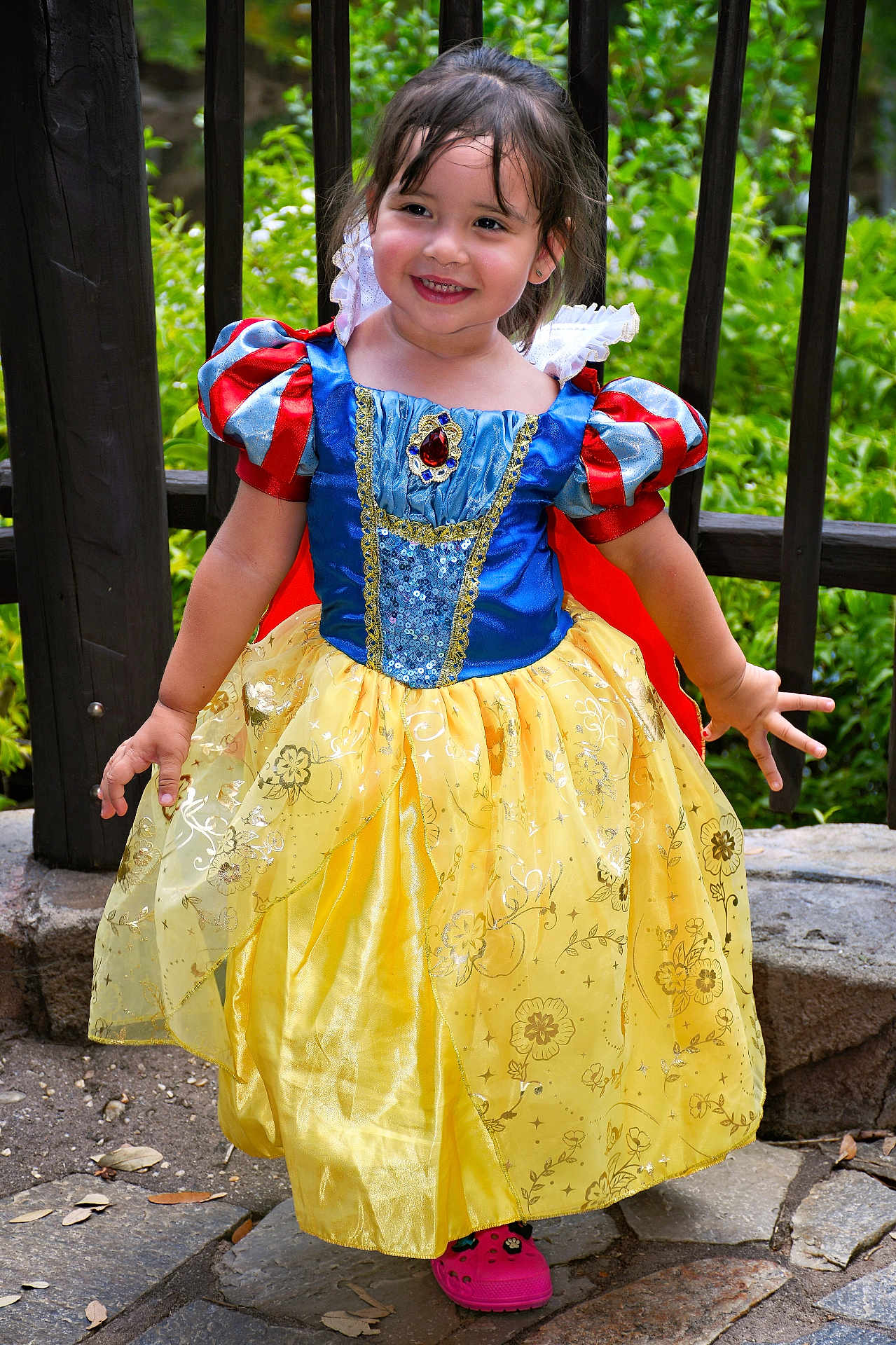 Aitana is registered to the contest to win money with this photo: child, girl, smiling, princess_costume, snow_white, dress, yellow_skirt, blue_bodice, red_sleeves, outdoor, greenery, stone_path, wooden_railings, happy, playful, portrait, cute, fashion, costume, childhood