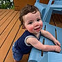 toddler, child, smiling, happy, outdoor, deck, wood, blue_chair, barefoot, curly_hair, face, person, summer, playful, leaning, clothing, tank_top, shorts, daylight, nature
