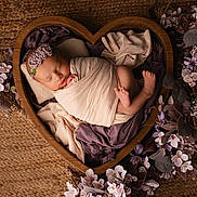 Mila participe au concours pour gagner de l'argent avec cette photo : newborn, baby, sleeping, wrapped, heart_shaped_bowl, wooden_bowl, flowers, purple_flowers, pink_flowers, blanket, headband, flower_headband, soft_lighting, portrait, infant, peaceful, cozy, cocoon, floor_rug, decorative