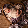 newborn, baby, sleeping, wrapped, heart_shaped_bowl, wooden_bowl, flowers, purple_flowers, pink_flowers, blanket, headband, flower_headband, soft_lighting, portrait, infant, peaceful, cozy, cocoon, floor_rug, decorative