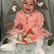 Rosalila is registered to the contest to win money with this photo: baby, child, smiling, headband, pink_coat, floral_dress, white_tights, carrot_toys, bunny_decorations, blanket, milestone, nine_months, cute, portrait, indoor, happy, sitting, infant, decor, celebration