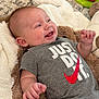 baby, infant, onesie, smiling, laughing, plush_blanket, toy, carpet, hand, face, cheeks, lying_down, gray_clothing, slogan_text, red_swoosh, happy, indoor, soft_texture, portrait, cute