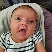 Léana a rejoint le concours — aidez-le/la à gagner de superbes lots ! baby, infant, face, tongue_out, striped_clothing, onesie, blue_stars, close_up, cute, child, person, portrait, indoor, soft_surface, resting, small_hands, young, adorable, expression, skin
