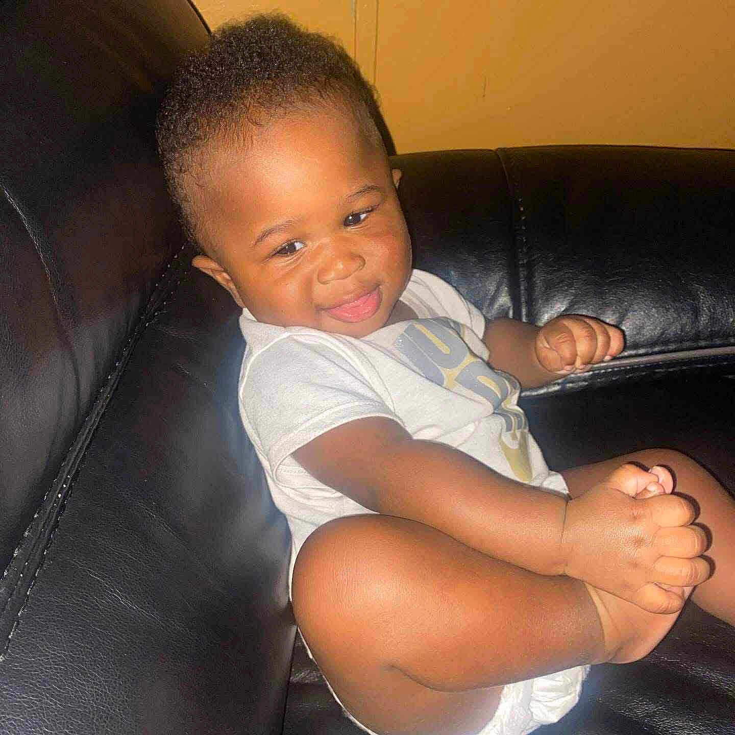 Key'Oir is registered to the contest to win money with this photo: baby, black_leather_couch, cheerful, child, cute, diaper, furniture, hand, head, holding_foot, indoor, infant, leg, room, sitting, skin, smiling, tongue_out, white_shirt, young