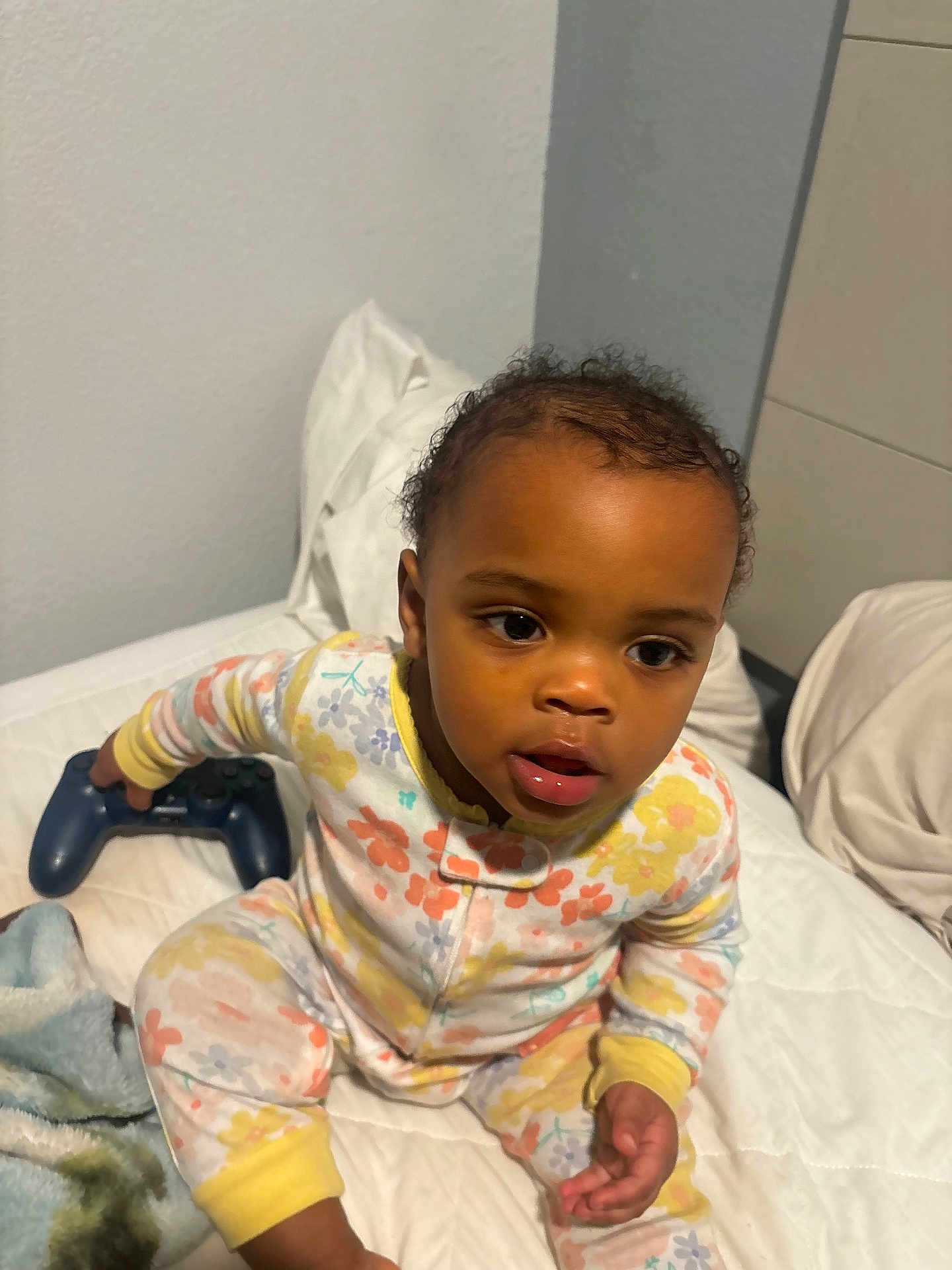 Emiyana joined the competition — help win amazing prizes! toddler, child, pajamas, bed, blanket, controller, video_game_controller, indoor, person, cute, young_child, curly_hair, expression, furniture, home, sitting, playing, cozy, colorful, comfort