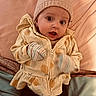 baby, child, infant, hat, knitted_hat, jacket, zipper, mittens, bed, blanket, pillow, soft_fabric, cute, wide_eyes, expression, indoor, person, clothing, portrait, lying_down