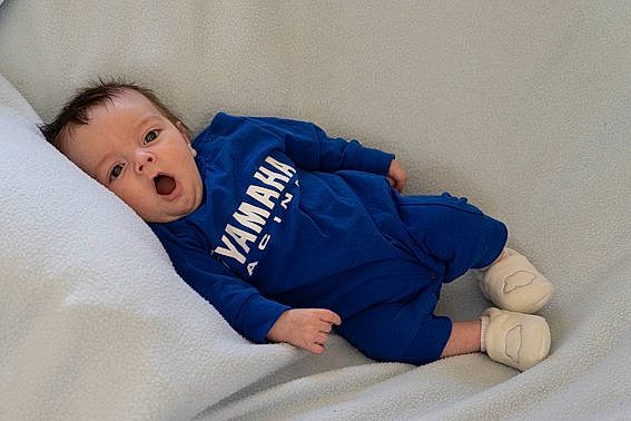 Rafaël participe au concours pour gagner de l'argent avec cette photo : baby, baby_products, baby_sleeping, baby_toddler_clothing, bedding, cheek, child, comfort, couch, electric_blue, facial_expression, knee, linens, person, room, sitting, skin, sleeve, surprise, toddler
