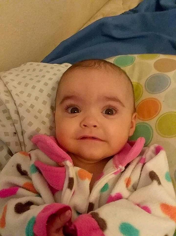 Ellie is registered to the contest to win money with this photo: baby, bedtime, blanket, cheek, child, eye, face, head, iris, linens, lip, mouth, nose, person, pink, skin, smile, textile, toddler