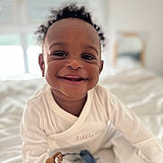 Ismaël a rejoint le concours — aidez-le/la à gagner de superbes lots ! baby, smiling, curly_hair, white_clothing, toy, teddy_bear, bed, blanket, indoors, child, happy, cute, portrait, person, infant, face, closeup, soft_light, comfort, playtime