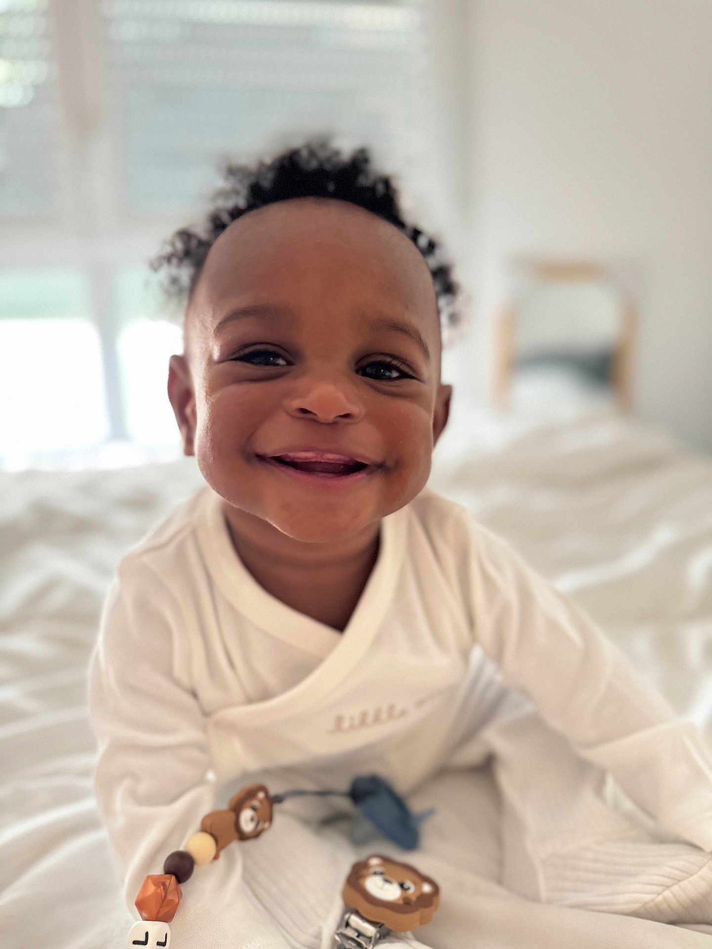 Ismaël a rejoint le concours — aidez-le/la à gagner de superbes lots ! baby, smiling, curly_hair, white_clothing, toy, teddy_bear, bed, blanket, indoors, child, happy, cute, portrait, person, infant, face, closeup, soft_light, comfort, playtime