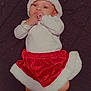 baby, blanket, celebration, child, christmas, cozy, cute, festive, hand_in_mouth, holiday, holiday_outfit, indoors, infant, lying_down, portrait, red_skirt, santa_hat, smiling_eyes, socks, white_top