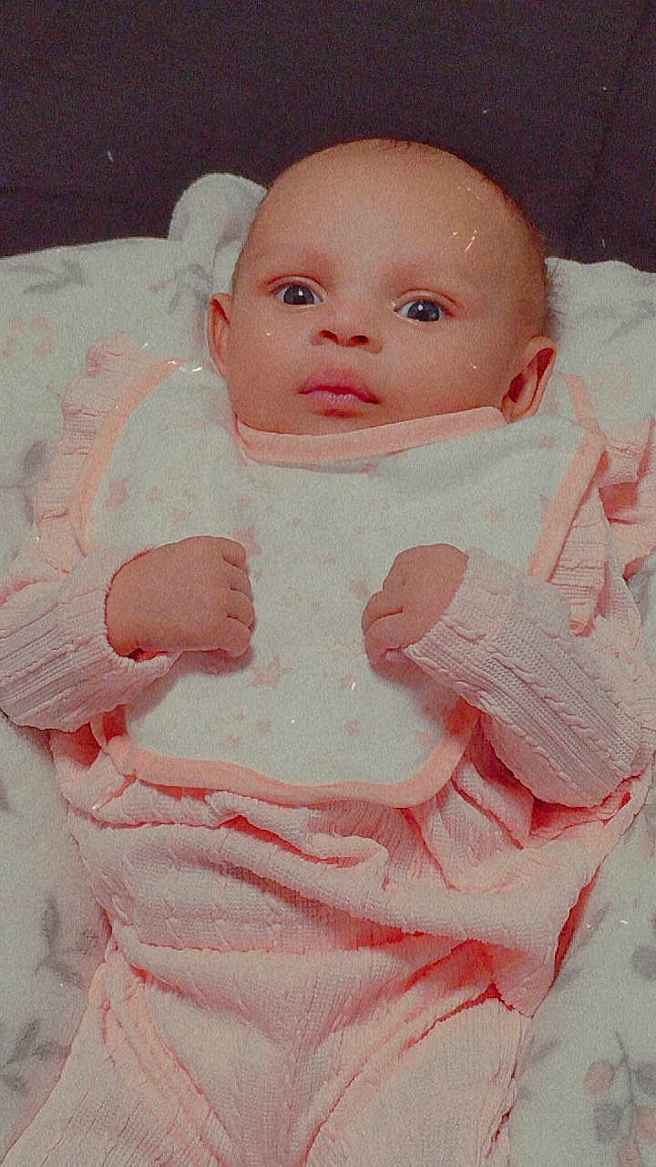 Aurora is registered to the contest to win money with this photo: baby, infant, pink_clothing, bib, blanket, fist, face, wide_eyes, cute, portrait, lying_down, soft_texture, child, newborn, indoors, cozy, hands, expression, baby_girl, clothing