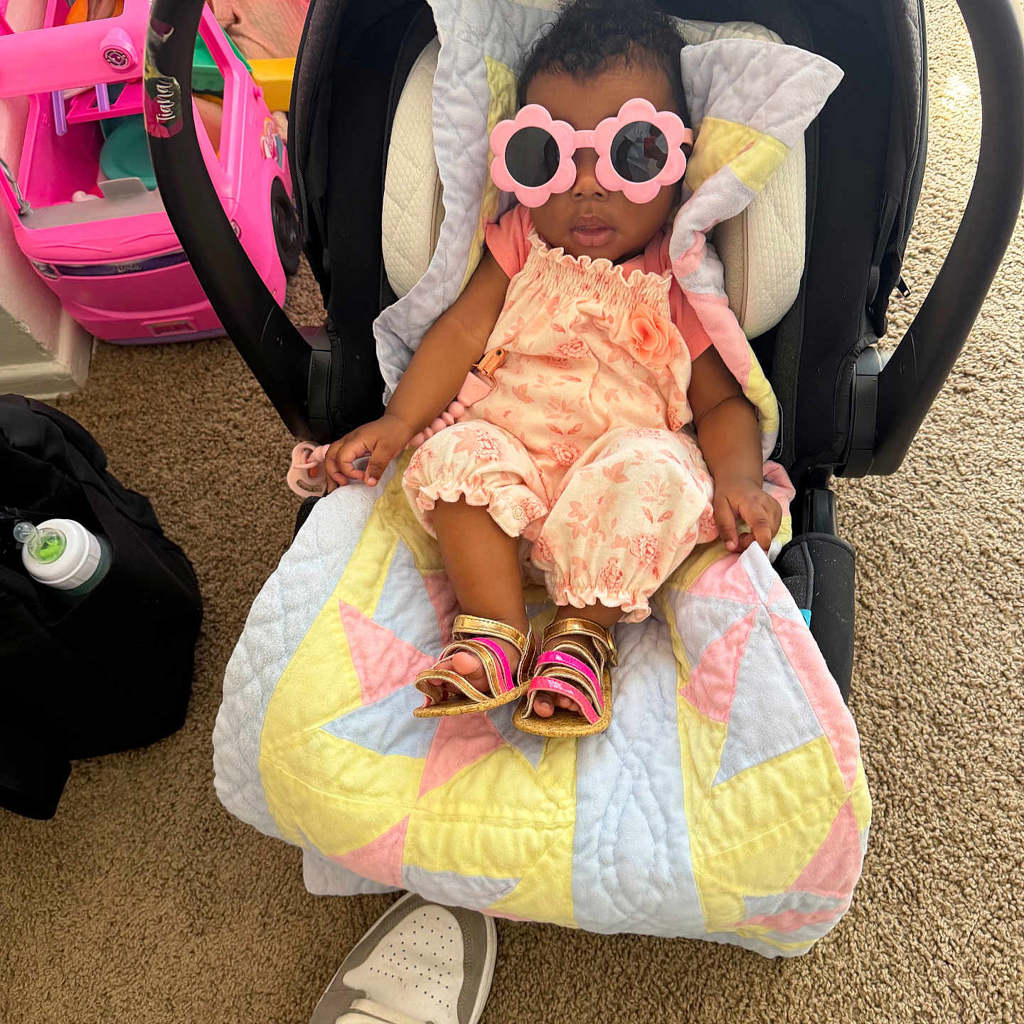 Zoya is registered to the contest to win money with this photo: baby, car_seat, sunglasses, pink, toy_car, doll, quilt, sandals, carpet, footwear, foot, indoor, child, person, plastic_toy, playroom, floor, accessory, clothing, cute
