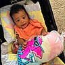 baby, child, cotton_candy, quilt, orange_bib, car_seat, colorful, smiling, happy, indoor, toy, food, pink, blue, yellow, fabric, footwear, person, portrait, cute