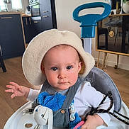 Marceau a rejoint le concours — aidez-le/la à gagner de superbes lots ! baby, child, cute, expression, floor, furniture, hat, indoor, infant, kitchen, living_room, person, playtime, plush_toy, seat, teether, toy, walker, white_clothing, wood_floor