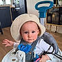 baby, child, cute, expression, floor, furniture, hat, indoor, infant, kitchen, living_room, person, playtime, plush_toy, seat, teether, toy, walker, white_clothing, wood_floor